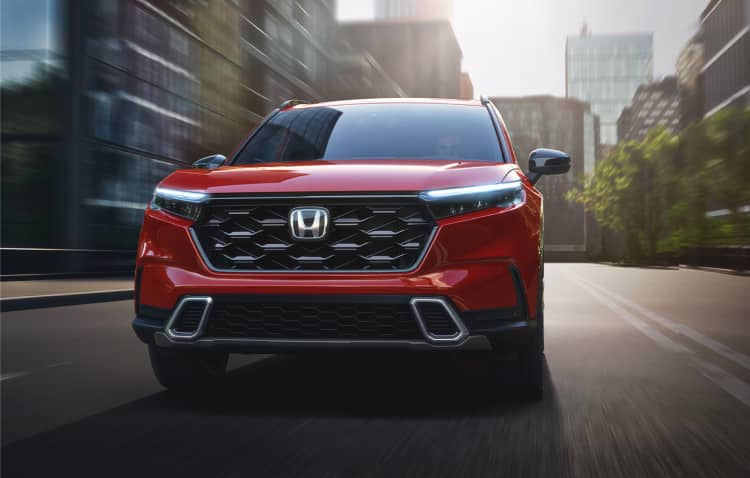 Straight front of 2025 CR-V Sport Touring in Radiant Red Metallic driving on downtown street.