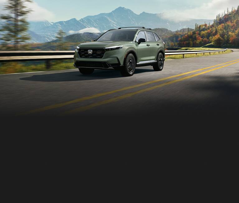 2026 Honda CR-V TrailSport Hybrid in Ash Green Metallic driving on a scenic mountain road (Compact Crossover SUV).