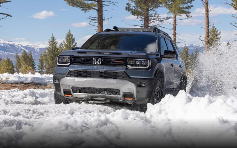 2027 Honda Passport TrailSport Elite in Smoke Blue Pearl front driving through deep snow in the mountains (Mid-Size SUV).